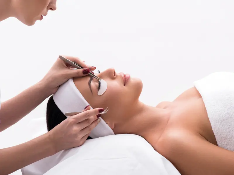 A lash artist applying extensions to a client lying on a treatment bed with eye pads