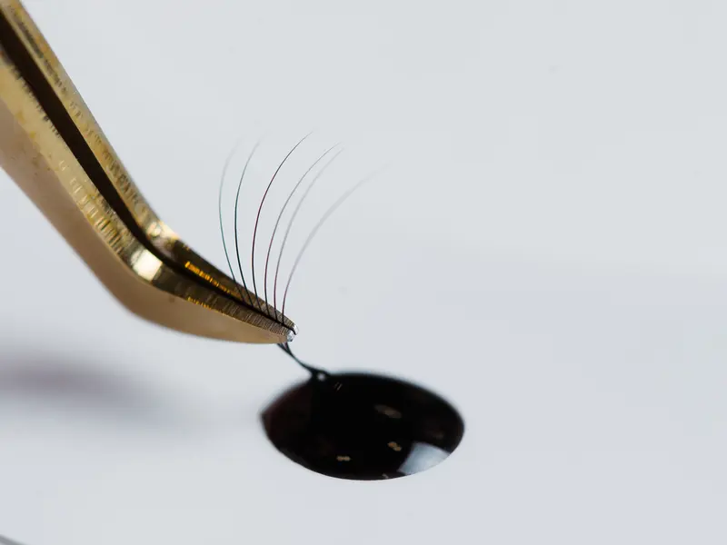 Gold tweezers holding lash extensions just dipped in a drop of lash glue